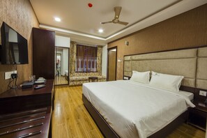 Habitación de hotel con una cama grande, un escritorio con televisión de pantalla plana, un ventilador de techo y una ventana con cortinas.
