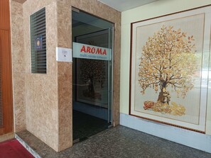 Entrada a un restaurante con un letrero que dice 'AROMA multi cuisine restaurant' y un letrero que indica 'NO MASK'.