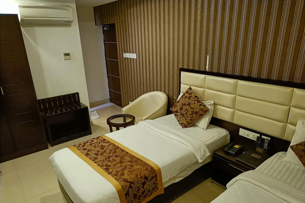 A hotel room with two beds, a chair, a small table, a wardrobe, and an air conditioning unit.
