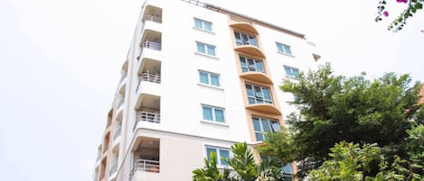 Un edificio de varios pisos con balcones, fachada plana y vegetación circundante.