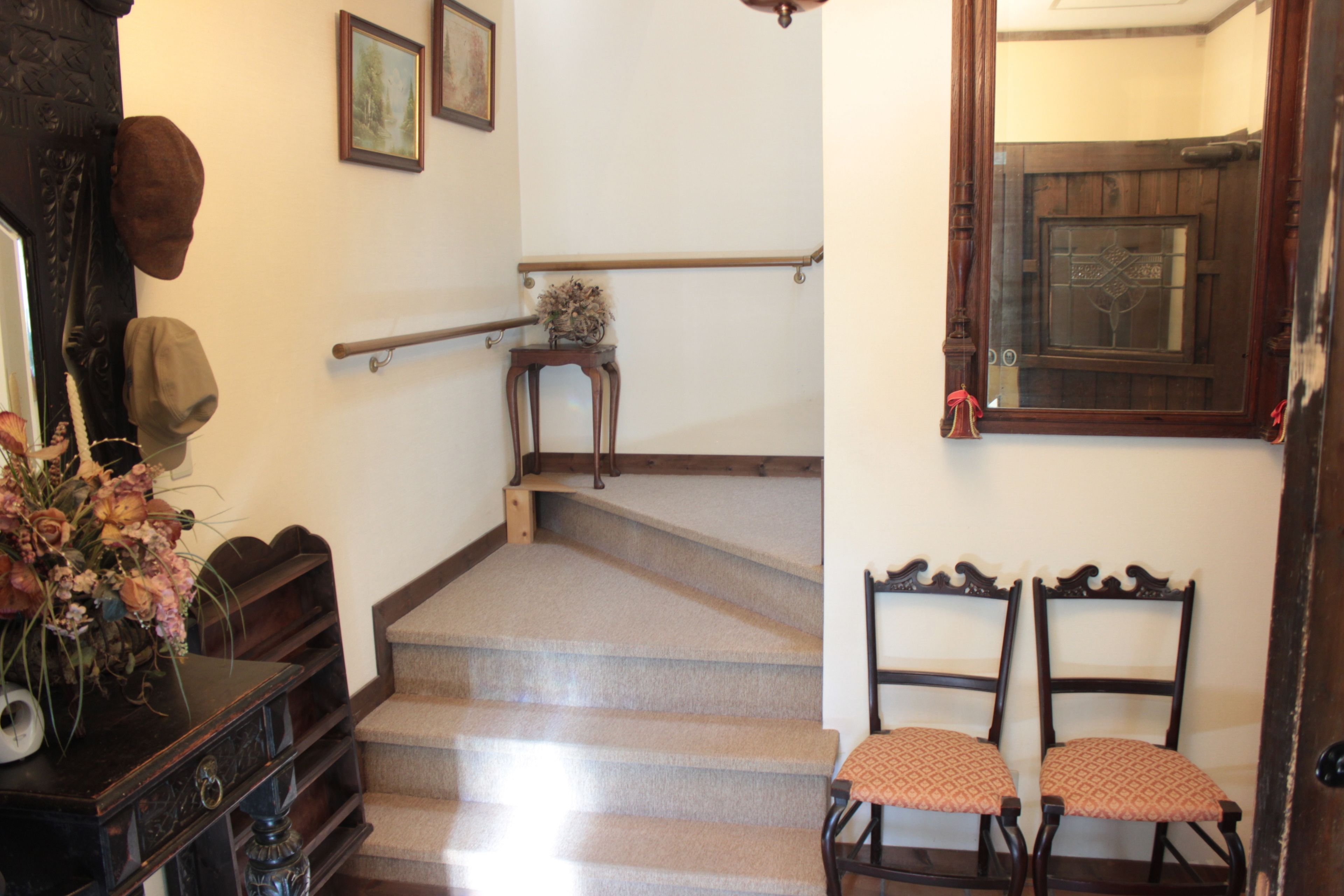 A staircase with a wooden handrail, a small table with a vase of flowers, and two chairs with patterned cushions.