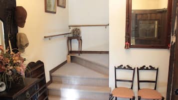 A staircase with a wooden handrail, a small table with a vase of flowers, and two chairs with patterned cushions.