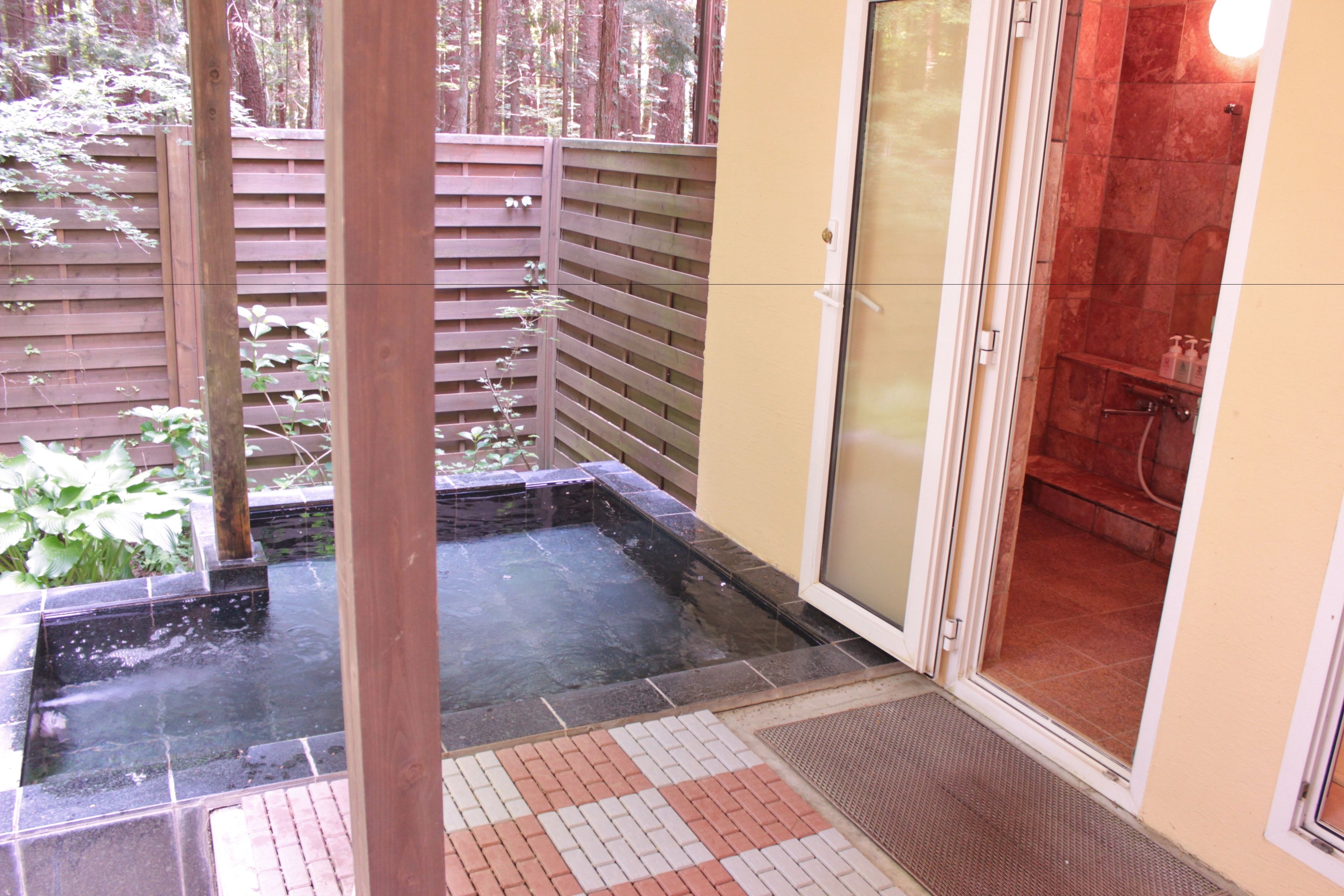 A spa area with a hot tub, a wooden fence, and a glass door leading to a shower room.