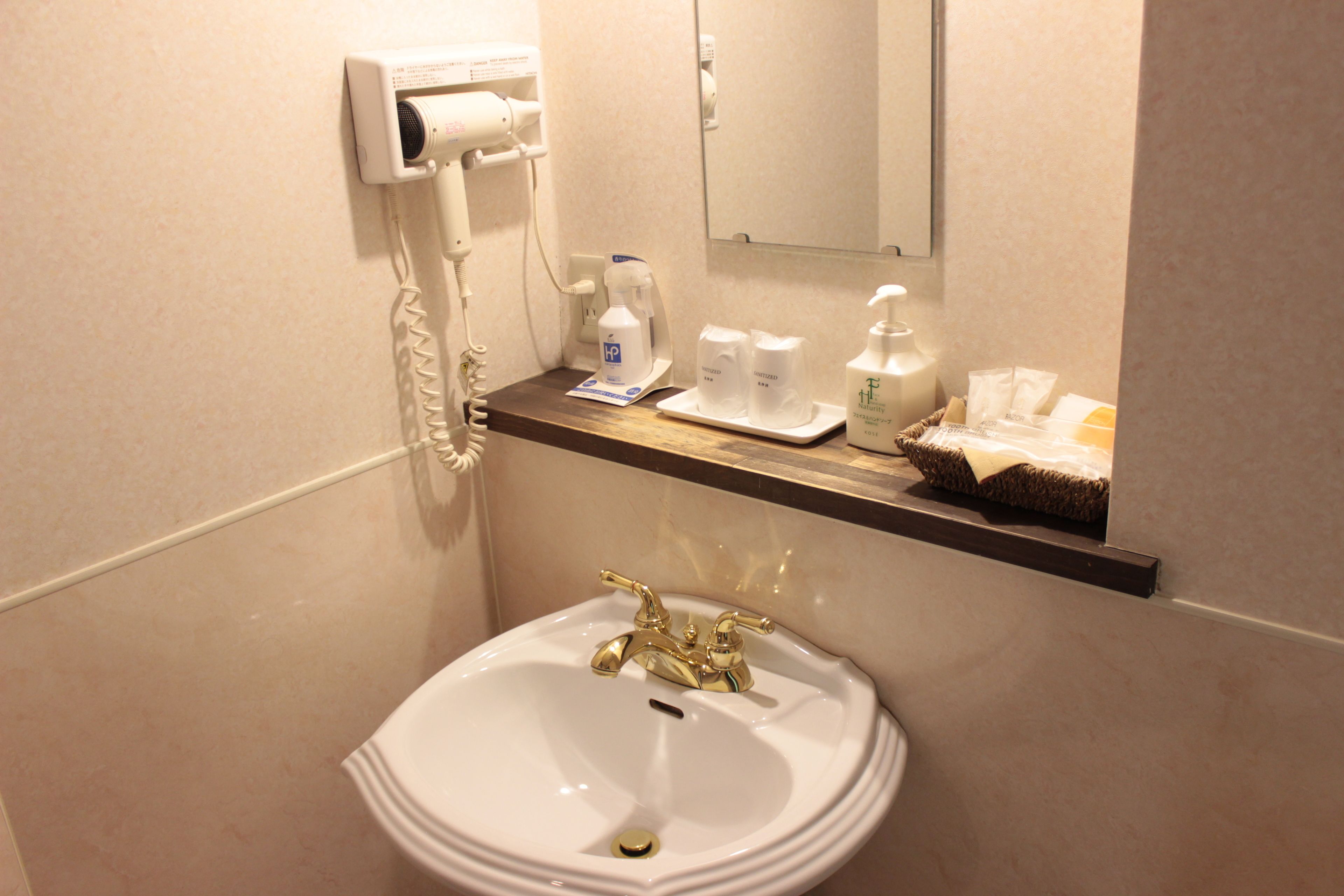 Un baño con lavabo, secador de pelo y artículos de aseo en un estante.