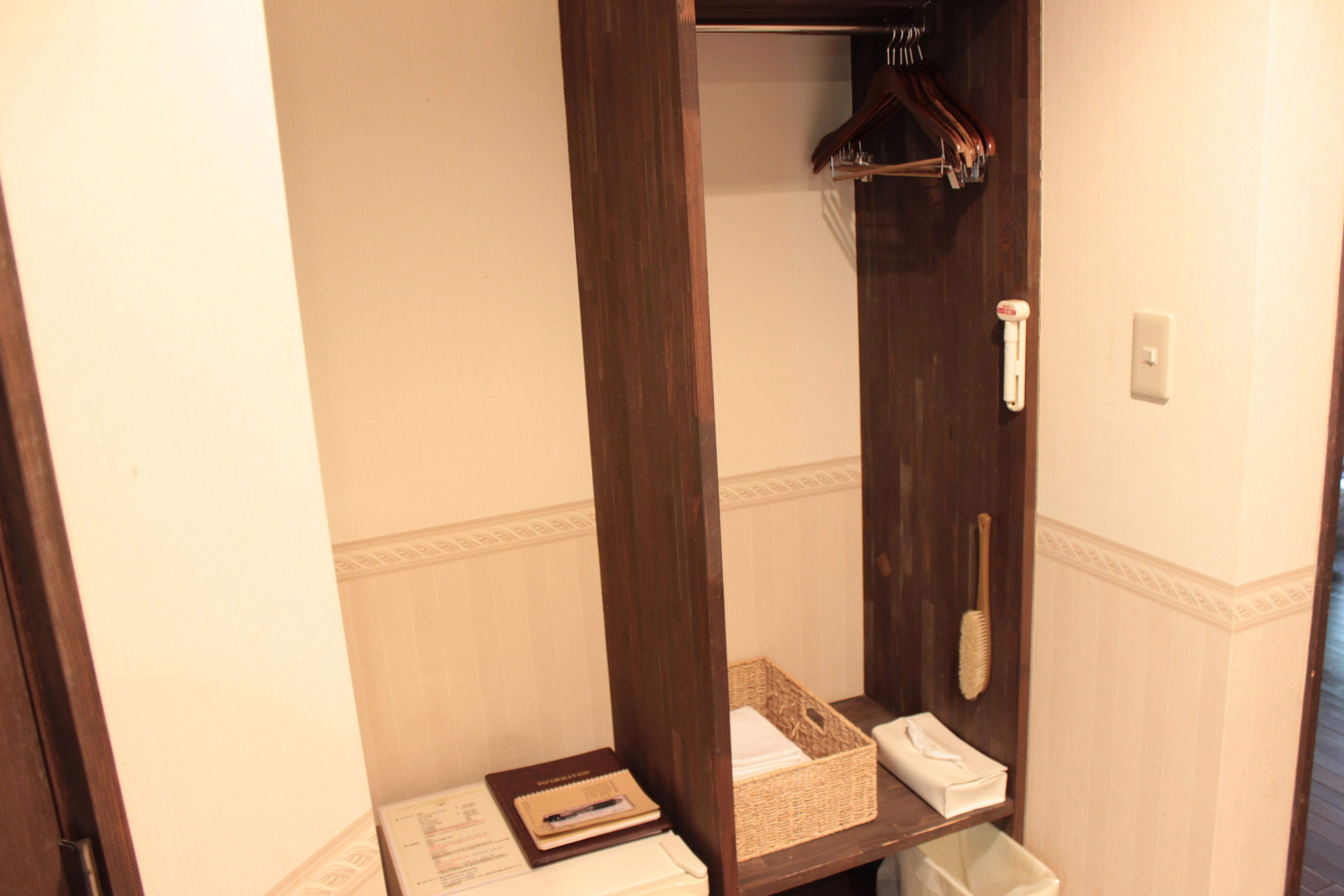 A small, enclosed bathroom with a wooden vanity, a hanging towel rack, a white trash bin, and a wicker basket on the counter.