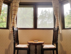 A room with two wooden chairs and a small table, a window with curtains, and patterned wallpaper. - Lumiere (Fujikawaguchiko)