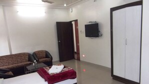 Una habitación de hotel con cama, sofá, sillón, televisor montado en la pared y armario.