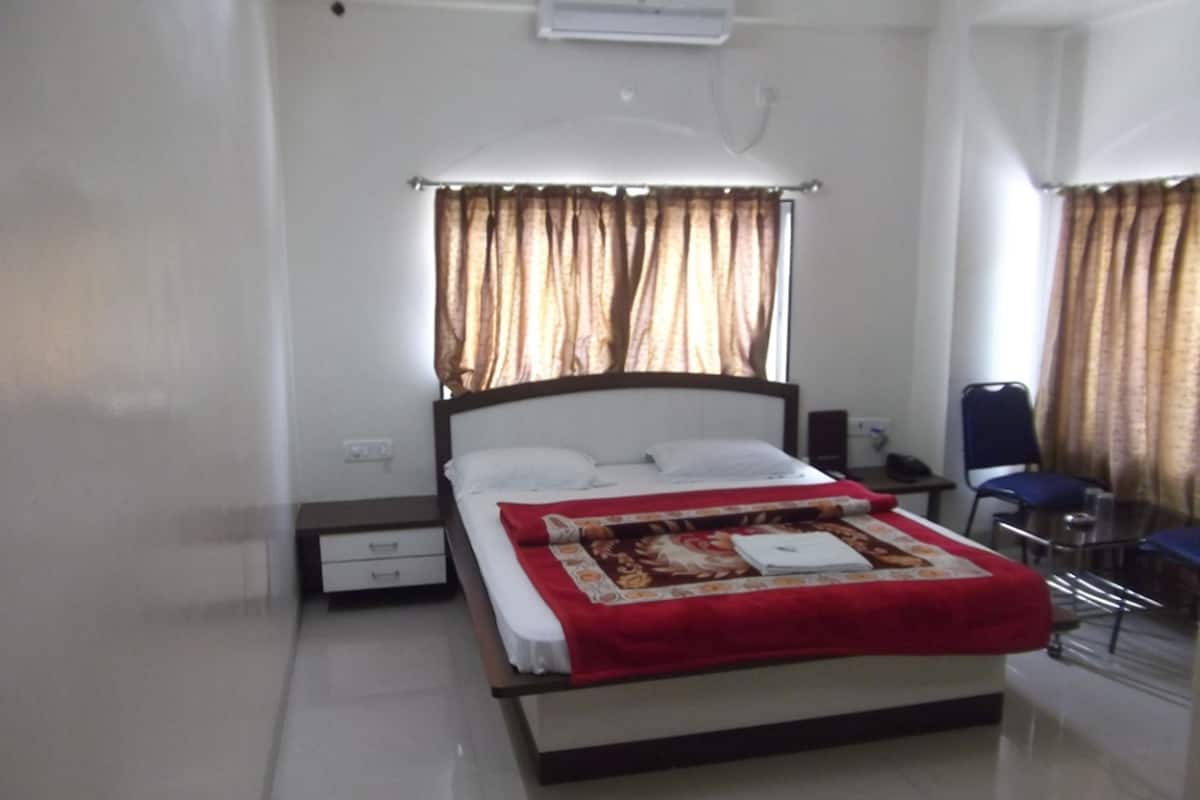 A neatly made bed with a red blanket, a bedside table, and a chair.