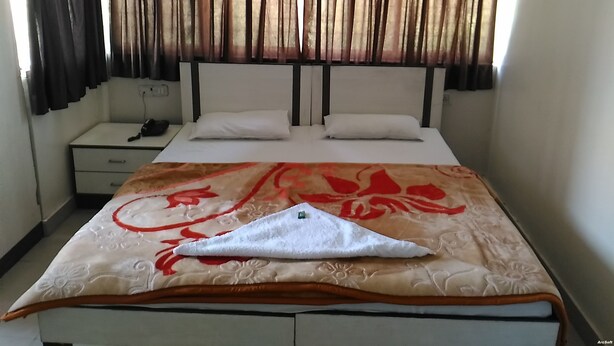 Una habitación de hotel con una cama, dos almohadas, una mesita de noche y cortinas.