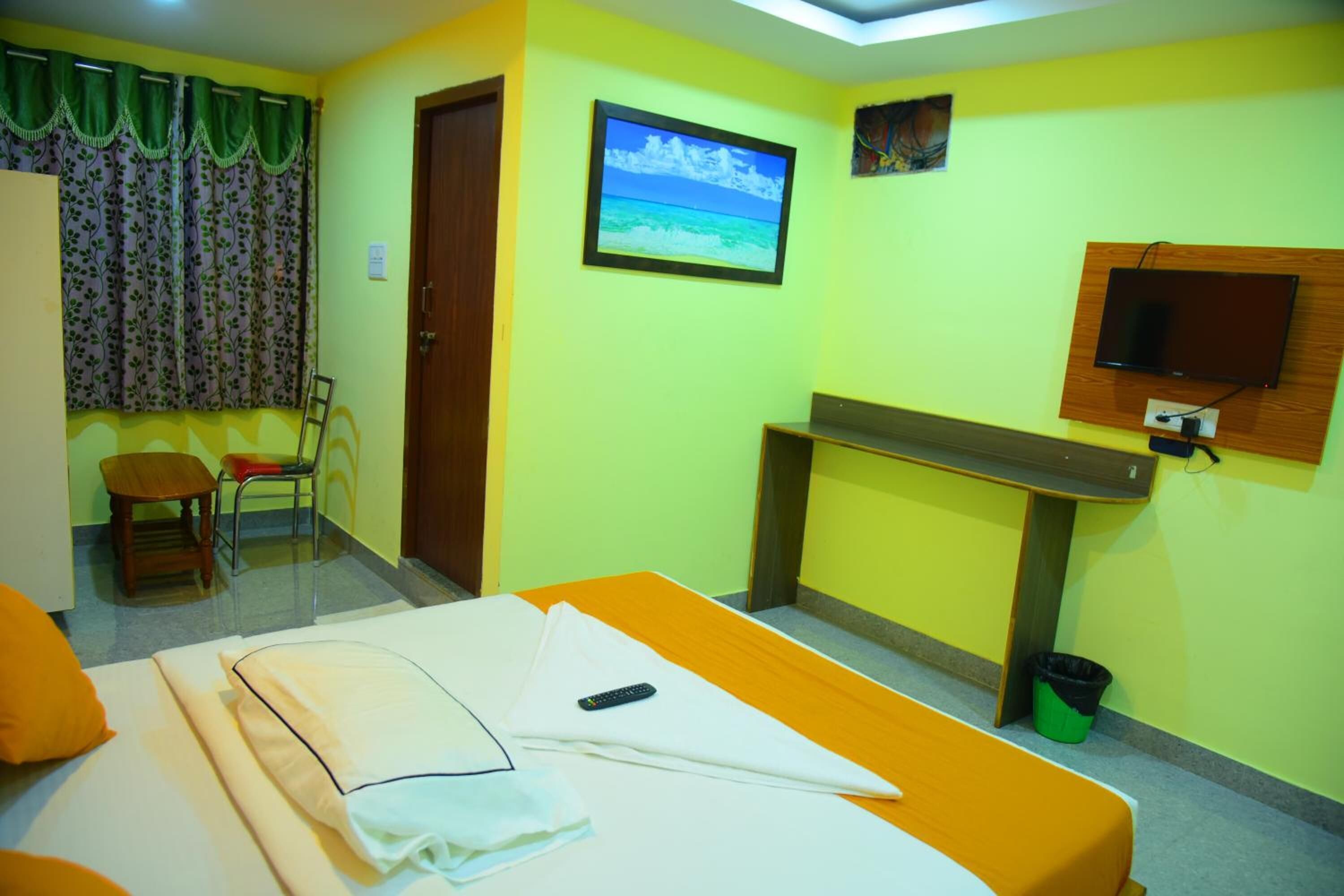 A hotel room with a bed, a desk, a chair, a television, and a painting on the wall.