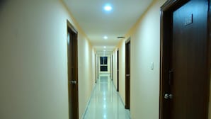 A long, narrow hallway with doors on both sides, a tiled floor, and recessed ceiling lights. - Housefinch Residency (Bengaluru)