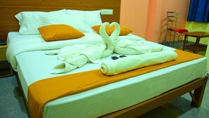 A neatly made bed with white and orange bedding, a heart-shaped towel arrangement, and a wooden headboard. - Housefinch Residency (Bengaluru)