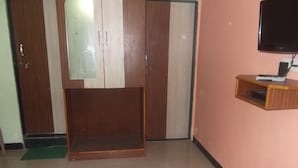 Una habitación de hotel con cama, televisión montada en la pared, un armario de madera y una puerta con espejo.