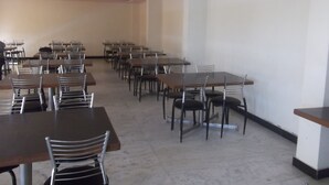 Una habitación amplia con varias mesas y sillas, un ventilador de techo y una pared lisa.