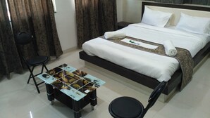 Quarto de hotel com cama, mesa pequena, duas cadeiras e cortinas.
