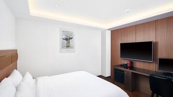 A modern hotel room with a large bed, a desk with a computer, a flat-screen TV, and a coffee maker.