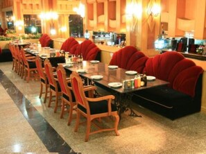 Un espace repas avec une longue table, des chaises à revêtement rouge et un sol recouvert d’une moquette.