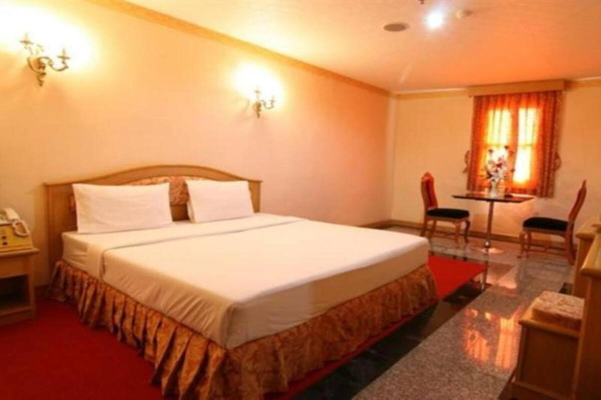 A hotel room with a large bed, a desk with two chairs, and a window with curtains.