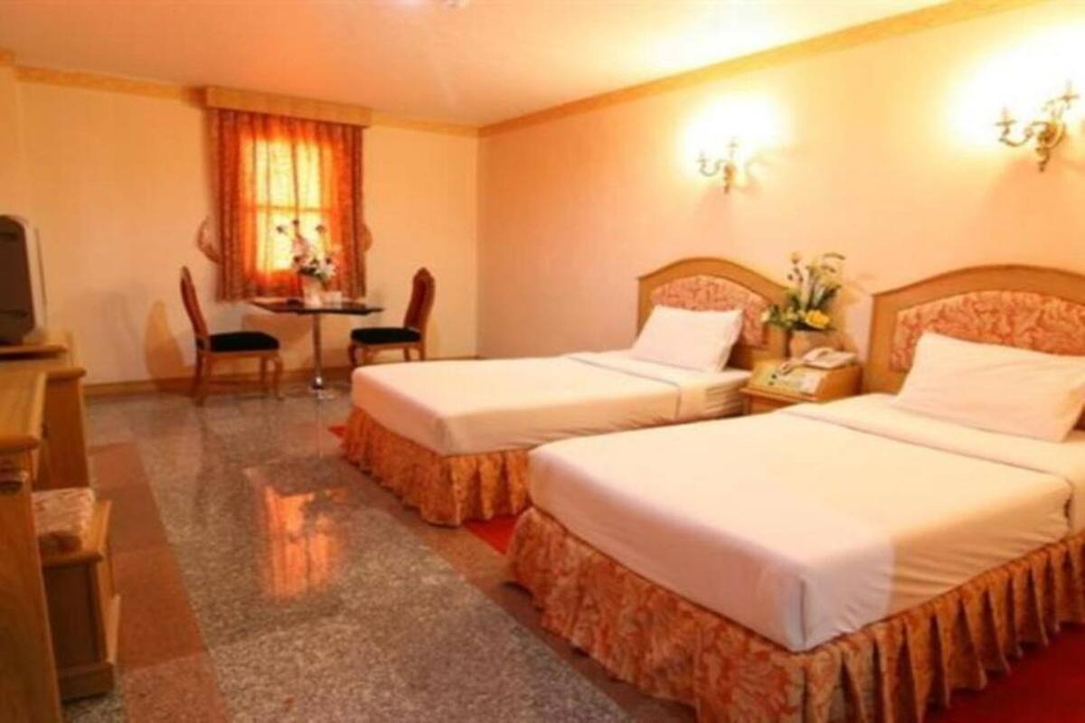 A hotel room with two single beds, a desk with a chair, a television, and a window with curtains.