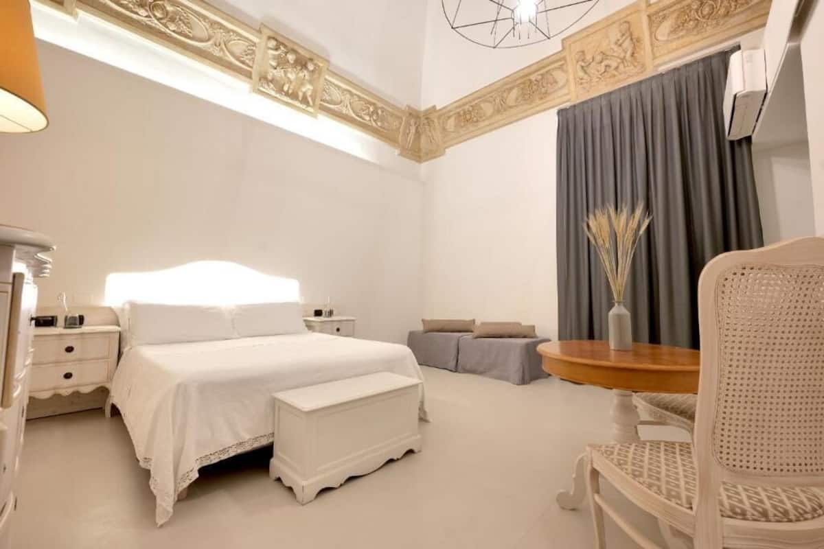 A hotel room with a large bed, a bedside table, a chair, and a small table with a vase.
