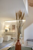 Una sala de estar moderna con un jarrón de espigas secas sobre una mesa de vidrio, un sofá blanco y una decoración de estilo minimalista.