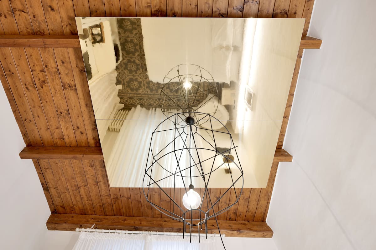 A ceiling with a geometric metal light fixture and a large mirror reflecting the room's ceiling and walls.