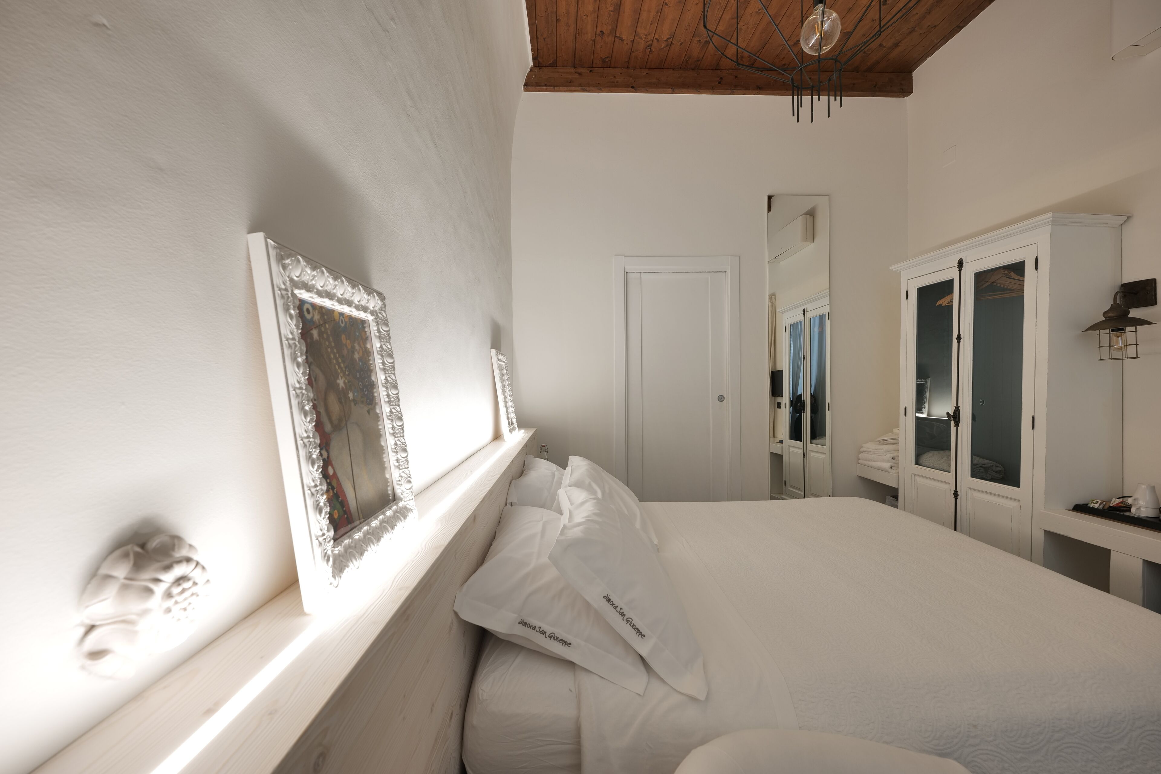 Un dormitorio con una cama grande, un armario, un espejo y una ventana con un marco.