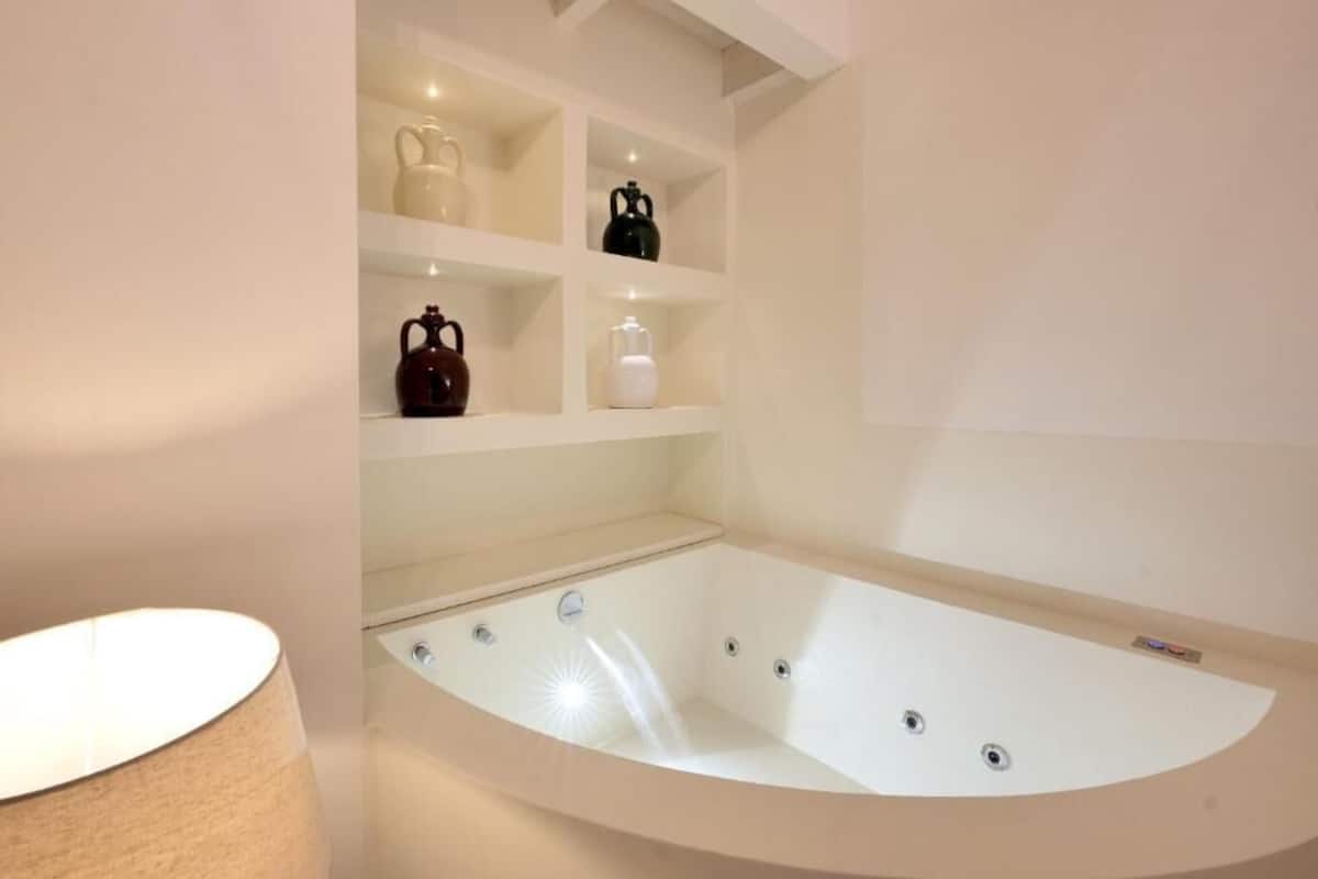A modern bathroom with a freestanding bathtub, a shelf with decorative items, and a lamp.
