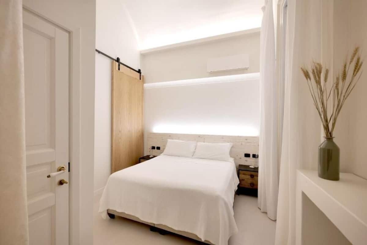 A bedroom with a bed, bedside tables, a wooden headboard, and a vase with dried plants.