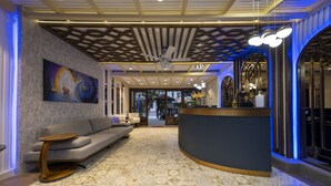 Un hall d’entrée moderne avec un comptoir d’accueil incurvé, un canapé gris, une moquette à motifs et un ventilateur de plafond.