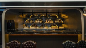 Un espace bar doté d’un comptoir en marbre, de fauteuils en cuir et d’étagères remplies de bouteilles d’alcool.