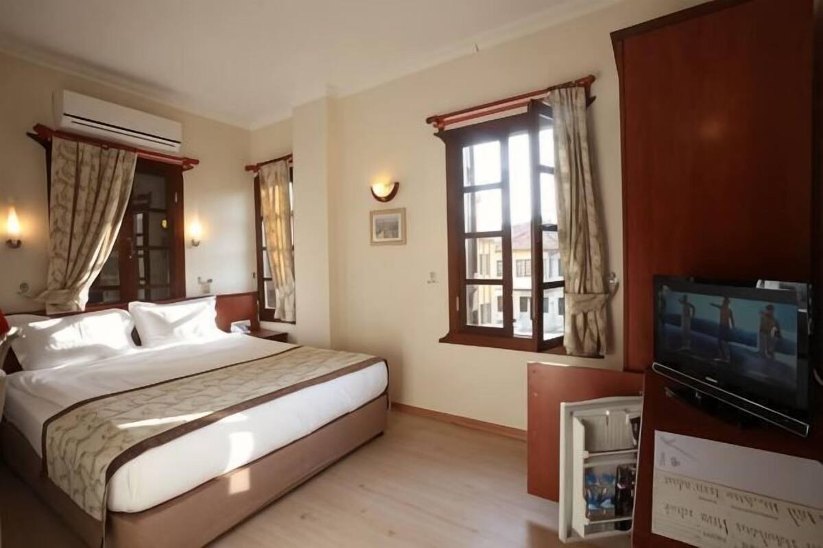 A hotel room with a bed, a TV, a desk, and a window with curtains.