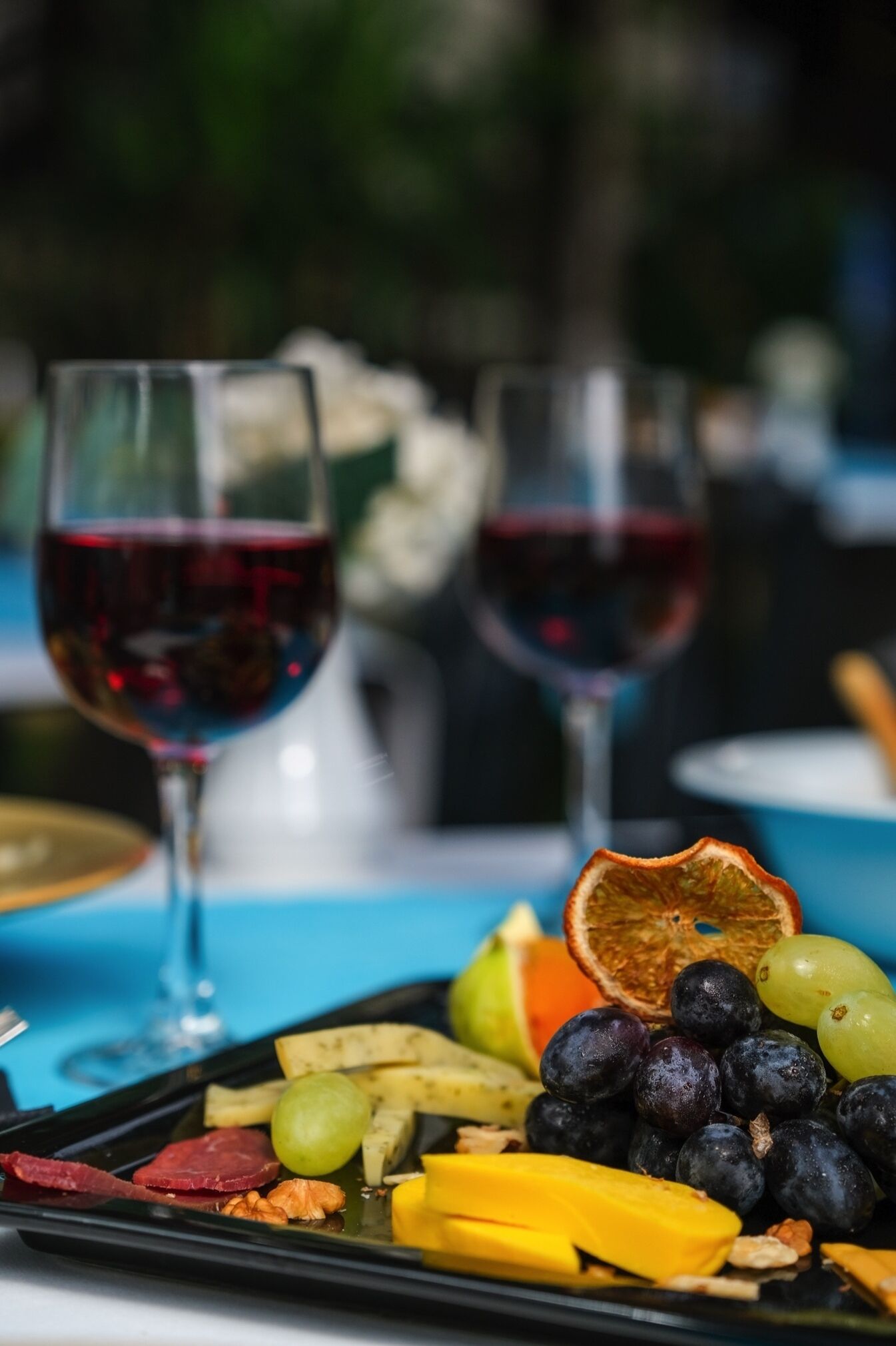Una mesa con una tabla de embutidos, dos copas de vino tinto y un mantel azul.