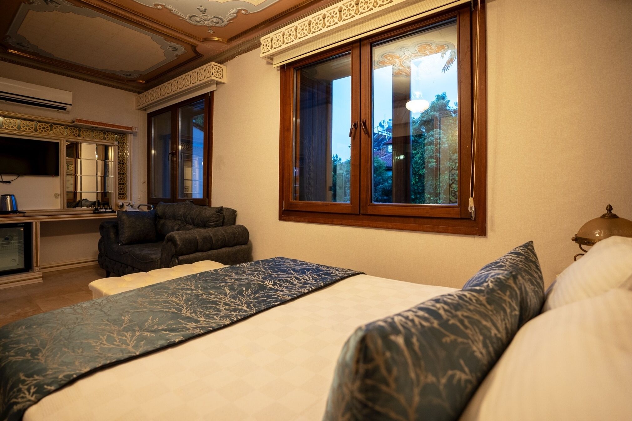 Ein Schlafzimmer mit einem großen Bett, einem Sofa, einem Schreibtisch mit Stuhl und einem Fenster mit Blick auf Gebäude.