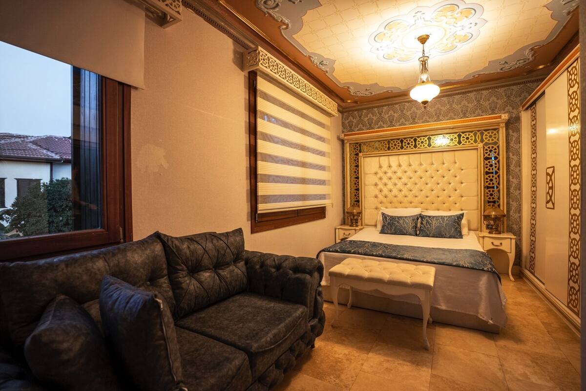 A bedroom with a large bed, a leather sofa, and a window.