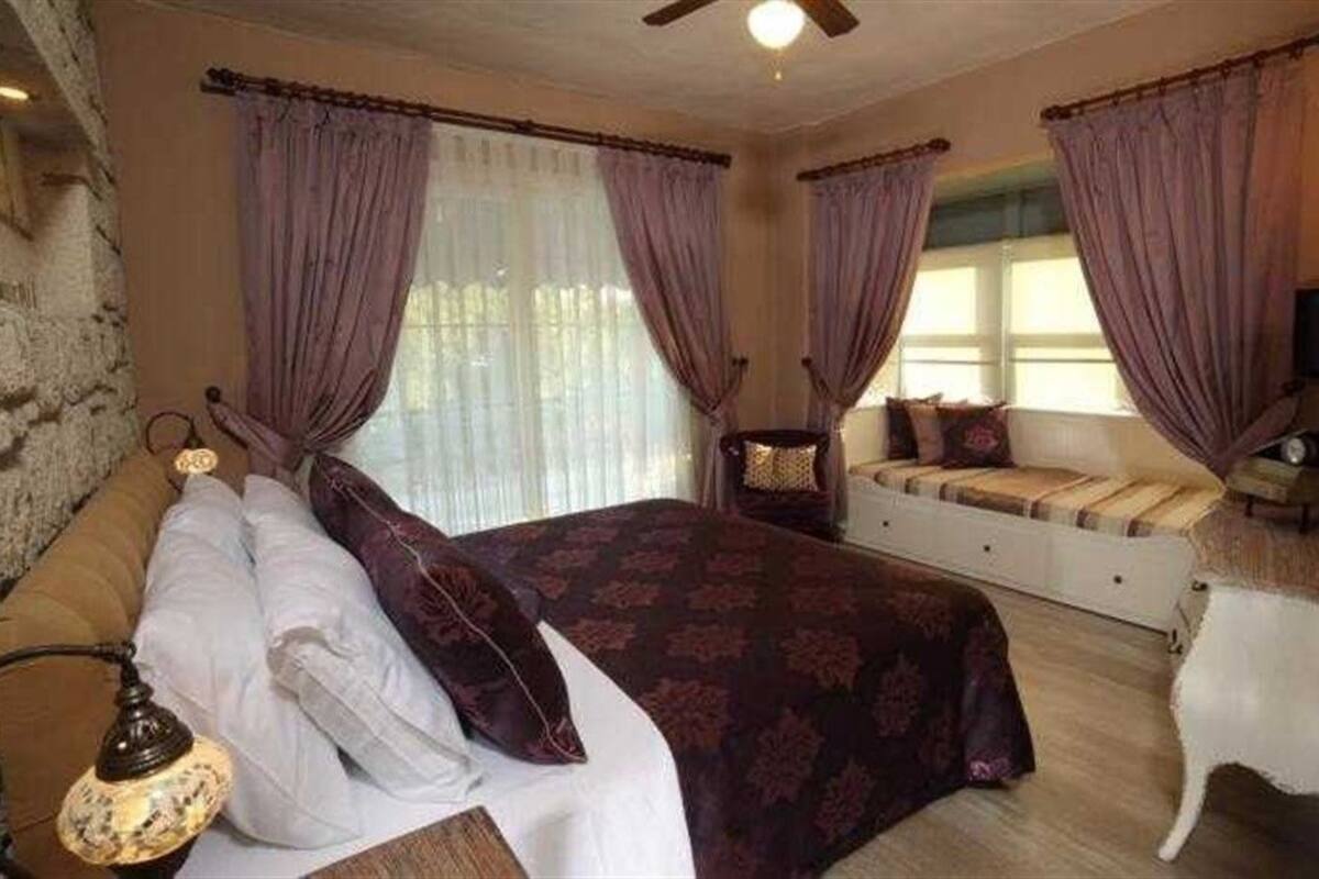 A bedroom with a large bed, a chair, a sofa, and a stone wall.