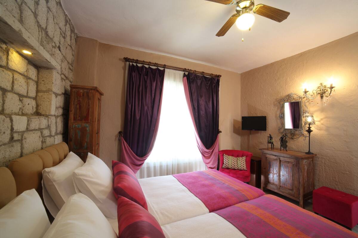 A bedroom with a stone wall, a bed with white and pink bedding, a red chair, a wooden cabinet, and a ceiling fan.