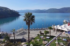 A coastal area with a marina, lounge chairs, and a palm tree. - İskelem Otel (Ula)
