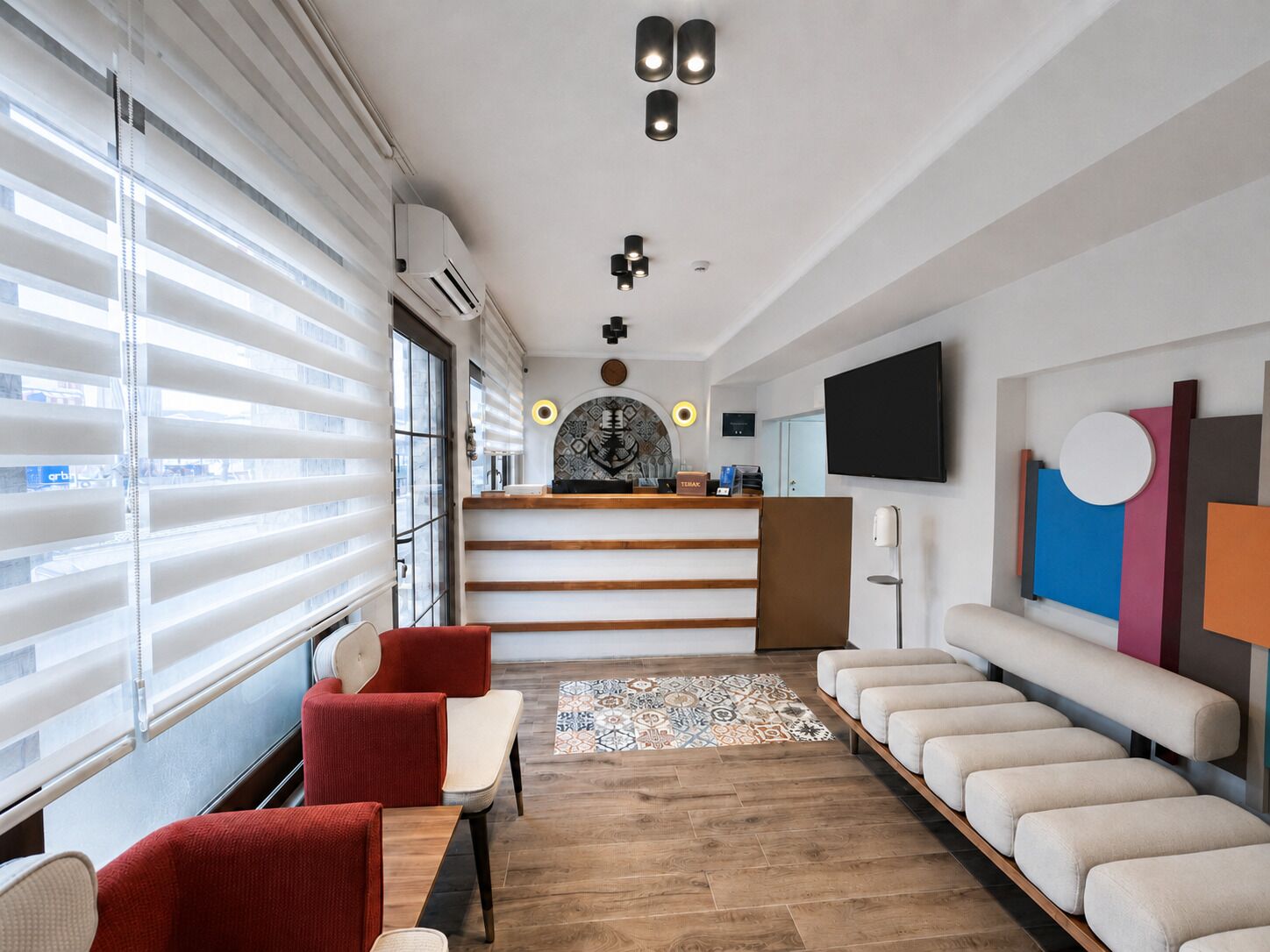 Een moderne hotellobby met een receptiebalie, een zithoek en grote ramen.