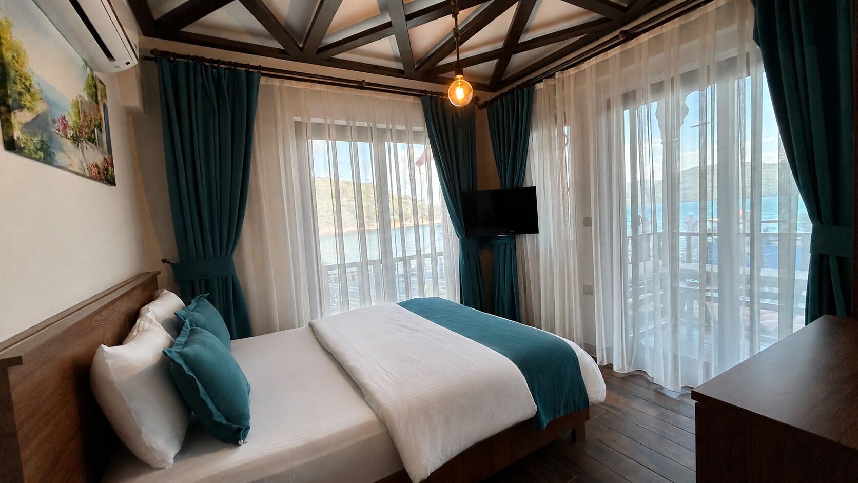 A hotel room with a bed, a TV, and a balcony with curtains.
