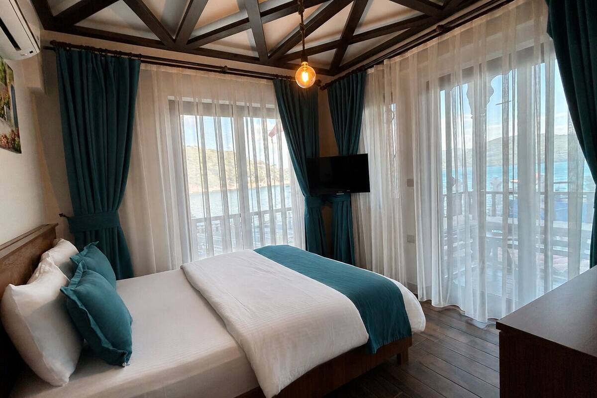 Habitación de hotel con cama, televisor y balcón con cortinas.
