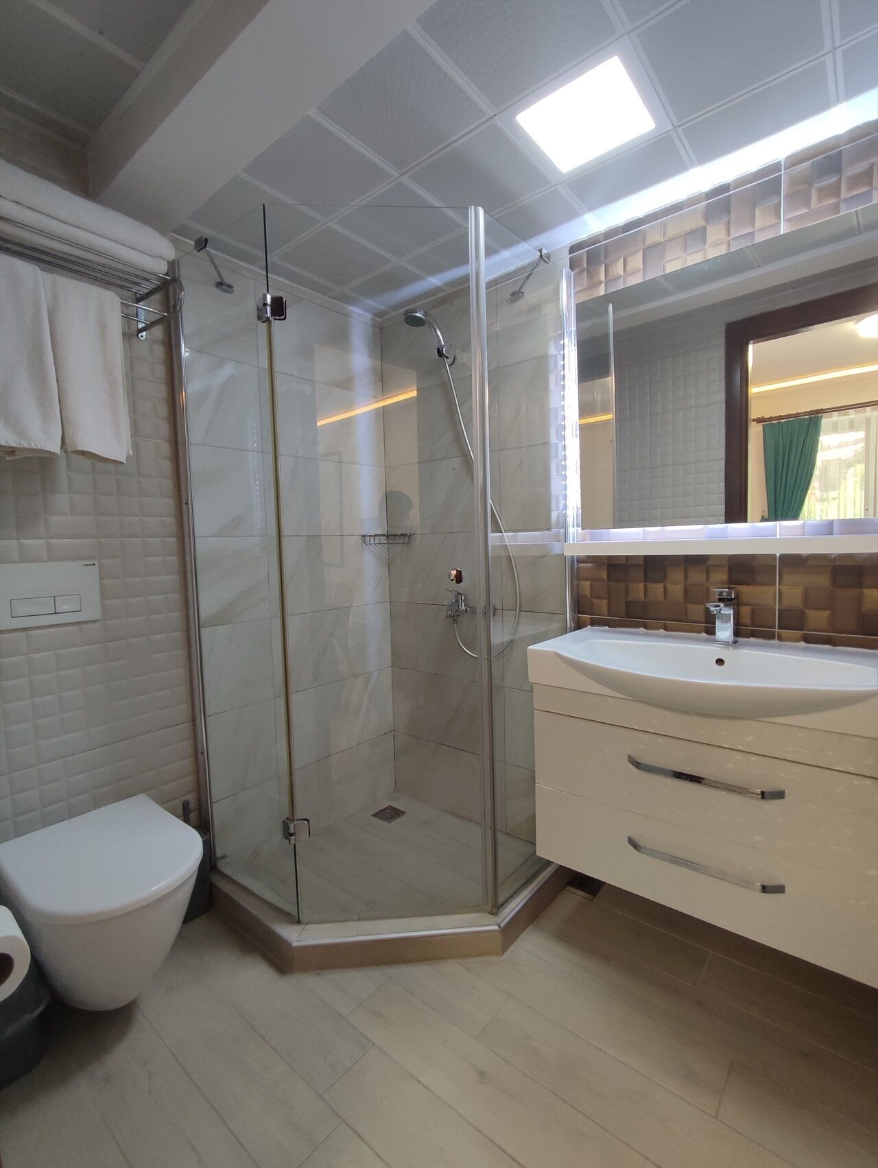 A bathroom with a glass-enclosed shower, a white toilet, a sink with a mirror above it, and a tiled floor.