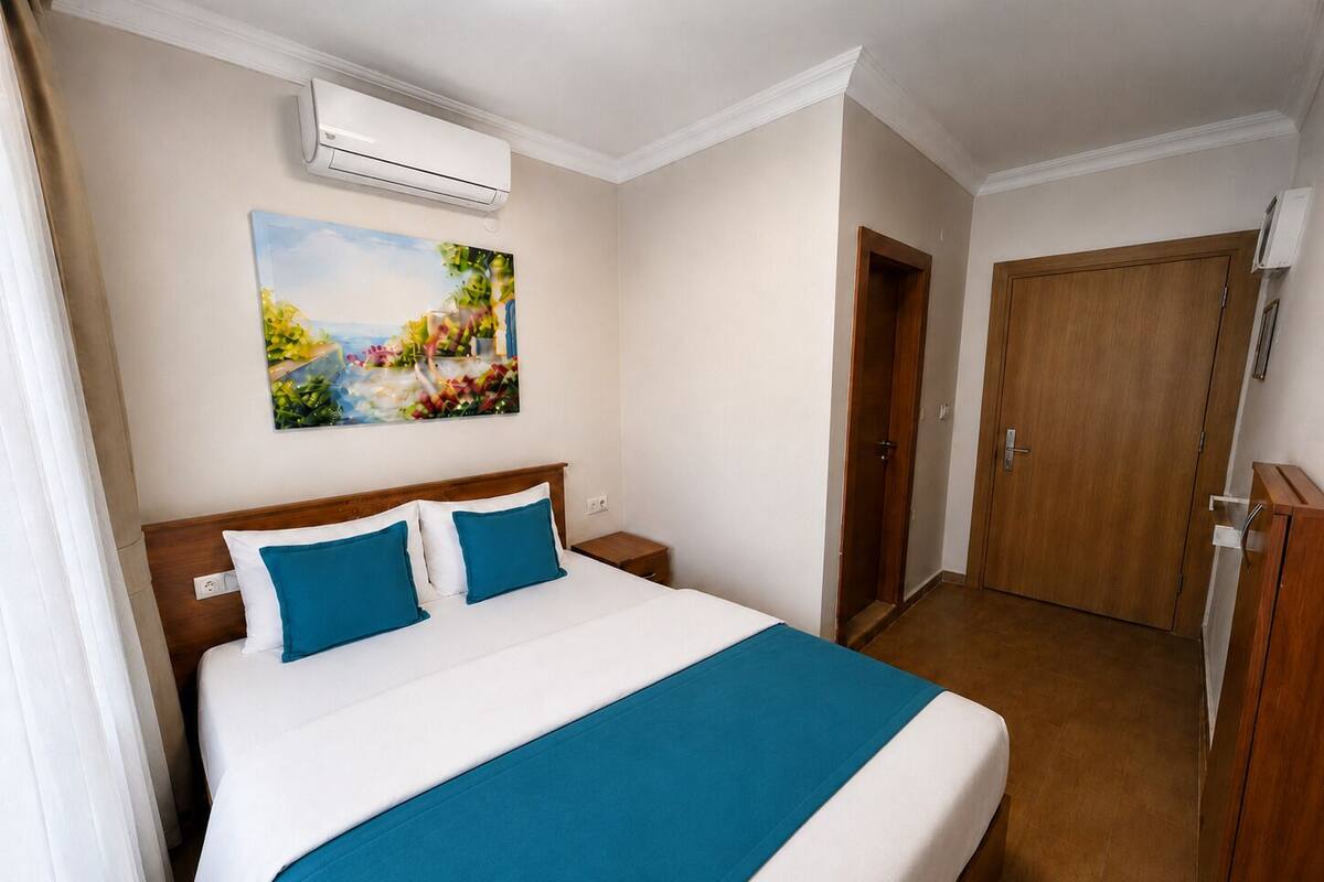 Una habitación de hotel con cama, un cuadro, unidad de aire acondicionado, armario y puerta.