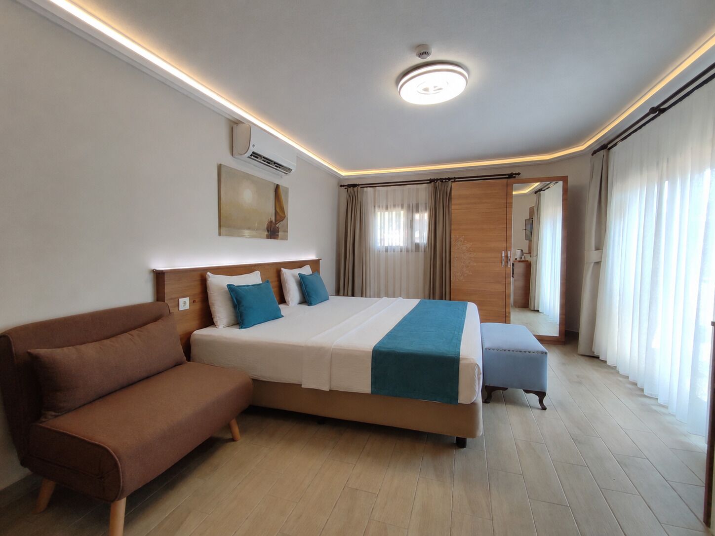 Una camera d'albergo moderna con un letto grande, un divano, un armadio in legno e una luce a soffitto.