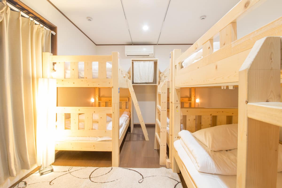 A room with bunk beds, a small window with curtains, and an air conditioning unit on the wall.