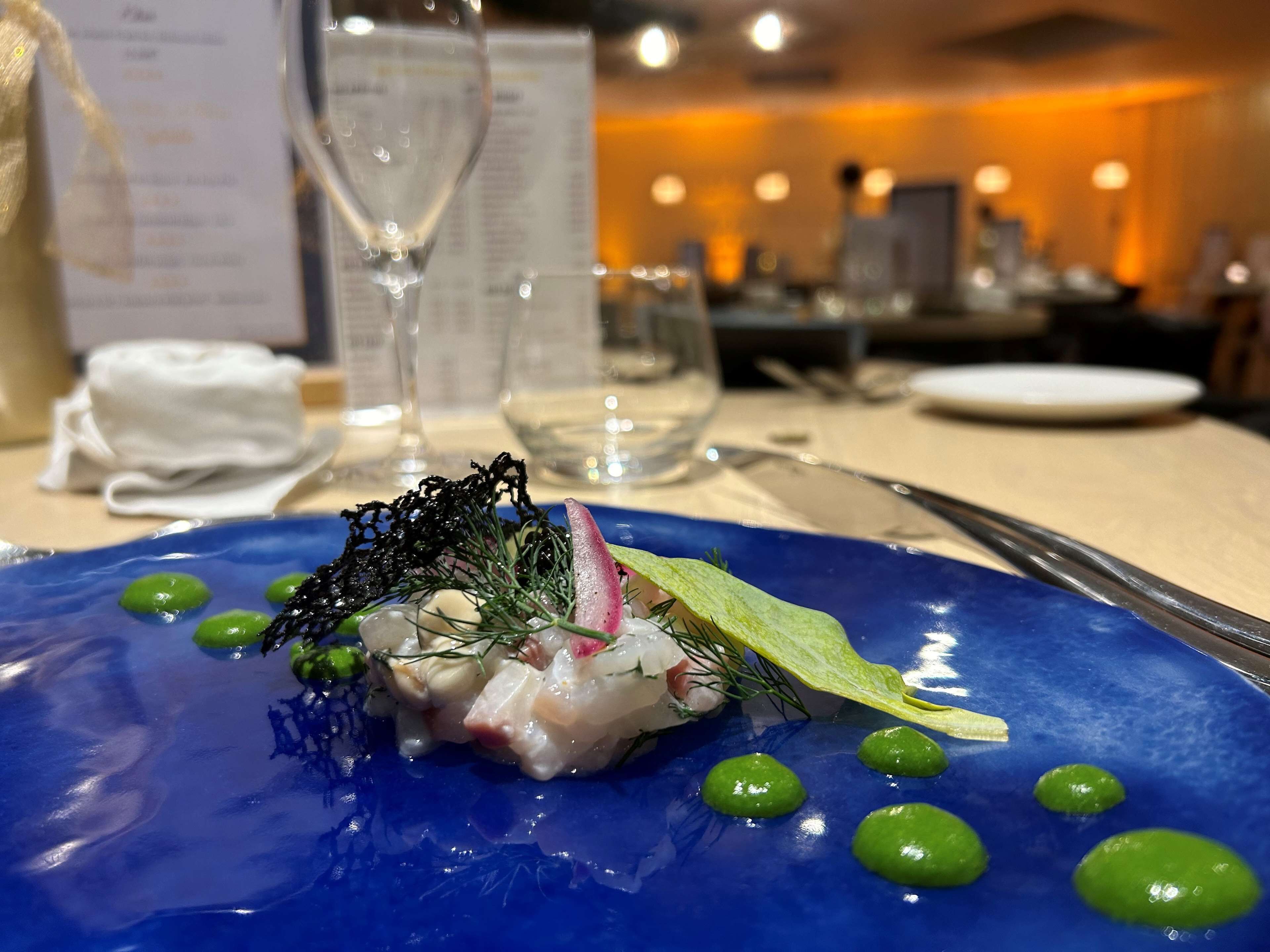 Une assiette bleue contenant un plat de fruits de mer, des petits pois verts et une serviette blanche, le tout posé sur une table.