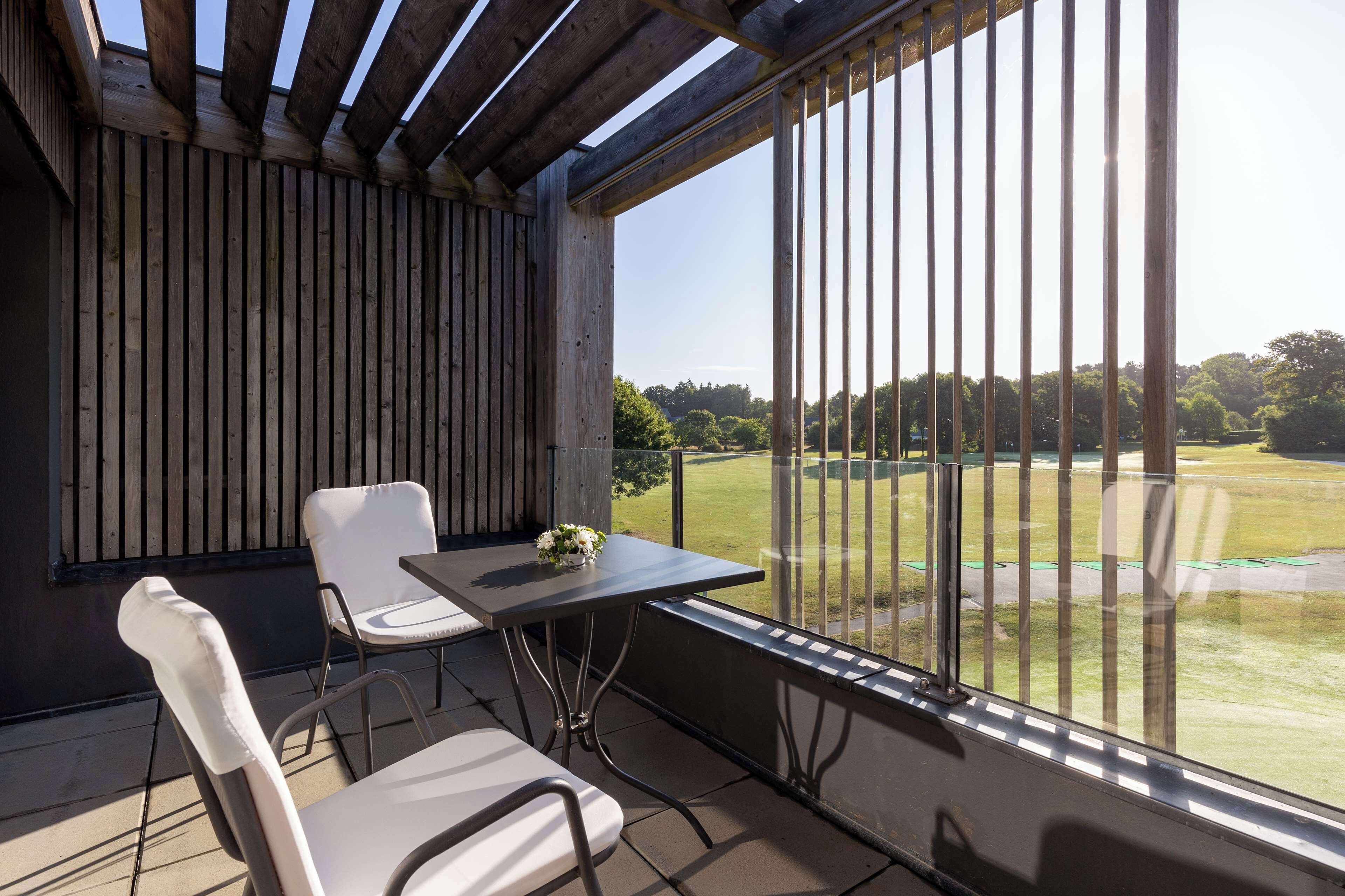 Een balkon met een tafel en stoelen, met uitzicht op een golfbaan.