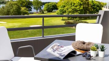 A balcony with a view of a golf course, a magazine, a pair of sunglasses, and two small potted plants.