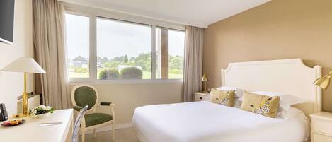 Habitación de hotel con una cama grande, un escritorio con lámpara, una silla y vistas a zonas verdes.