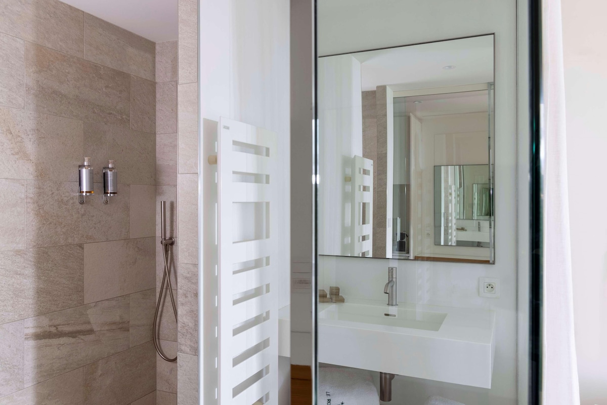 A modern bathroom with a glass shower enclosure, a white vanity with a mirror, and a beige tiled wall.